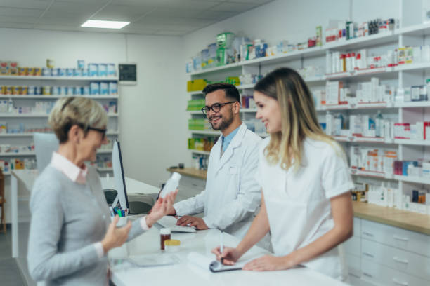 istock Male pharmacist working on a computer while female pharmacist is giving prescription medications to senior patient 1357548563