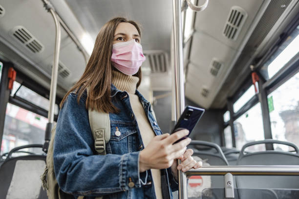 istock Woman with a protective face mask in a bus, using smart phone 1357550107