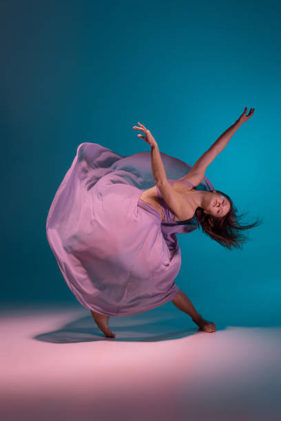 istock One young flexible contemp dancer in lilac dress dancing isolated on gradient blue white background in neon. 1357550149