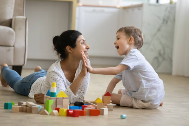 Happy nanny giving high five praise to excited preschool kid Happy nanny giving high five praise to excited preschool kid boy for completing toy tower on warm floor. Indian babysitter and kid playing at home, constructing building from small wooden blocks asian nanny stock pictures, royalty-free photos & images
