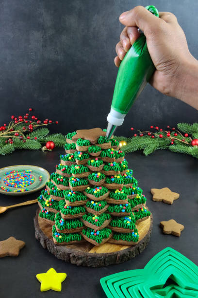 積み重ねられたジンジャーブレッドスタークッキーから組み立てるクリスマスツリーの画像は、認識できない人による緑色のバターアイシング渦巻き、多色のキャンディボールの装飾、黄色� - star shape christmas ornament heap stack ストックフォトと画像
