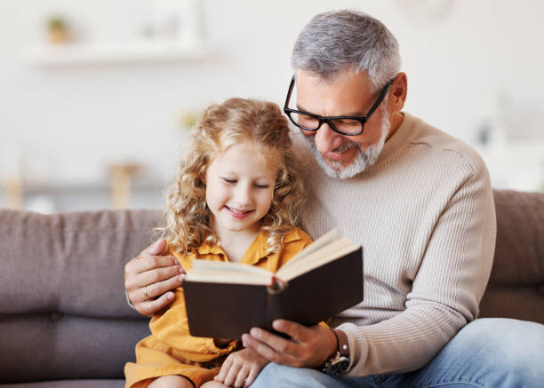 かわいい女の子の孫娘は、肯定的な先輩の祖父と本を読んで - adult caucasian senior adult family ストックフォトと画像