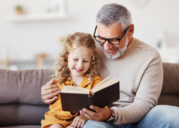 neta zinha fofa lendo livro com avô idoso positivo - listening child grandfather family - fotografias e filmes do acervo