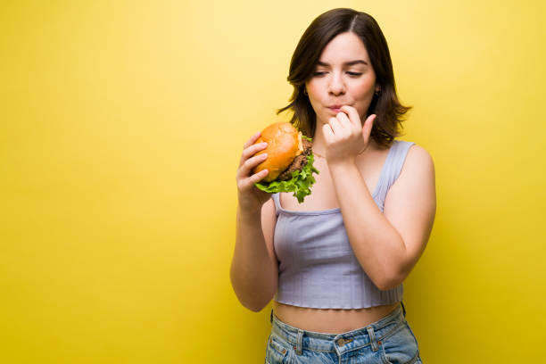 голодная женщина держит бургер - finger in mouth стоковые фото и изображения
