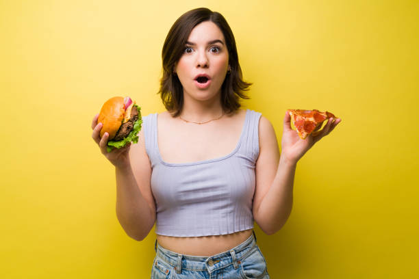 istock Attractive woman holding a burger and pizza 1357558682