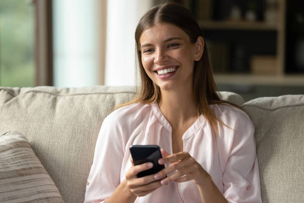 istock Dreamy attractive smiling young woman using cellphone. 1357564376
