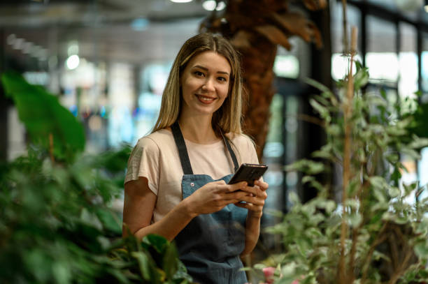 Florist using smartphone while surrounded with flowers and plants in a flower shop