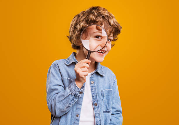 Cheerful boy with magnifying glass looking at camera stock photo