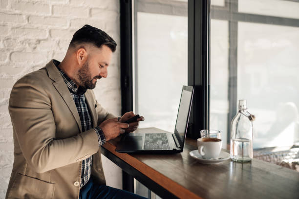 istock Businessman using smartphone and a laptop while drinking coffee in a cafe 1357572487