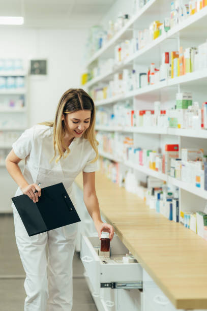 istock Beautiful female pharmacist working in a pharmacy while checking medications on the shelf 1357572577