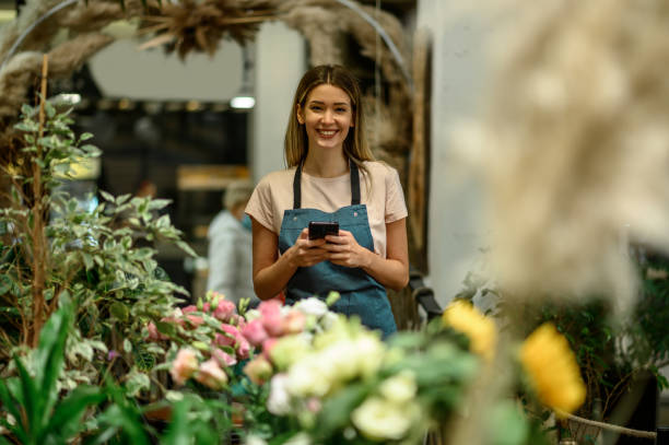 istock Florist using smartphone while surrounded with flowers and plants in a flower shop 1357572586