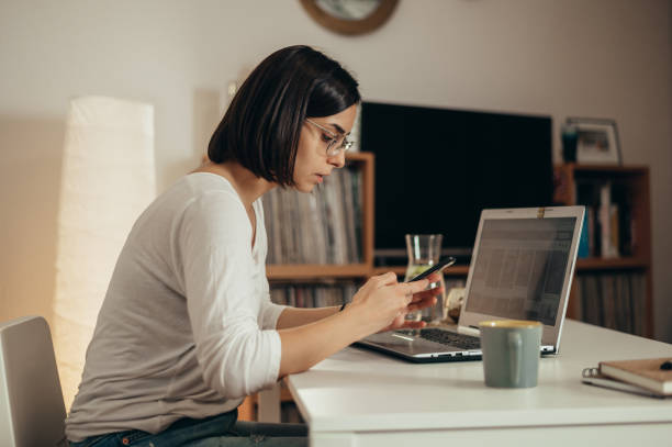 istock Beautiful woman using smartphone and a laptop while working from home 1357572600