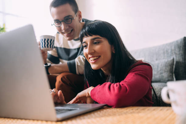 una mujer curiosa que desplaza algo en su computadora portátil mientras su esposo está mirando - simplicity using computer women computer equipment fotografías e imágenes de stock