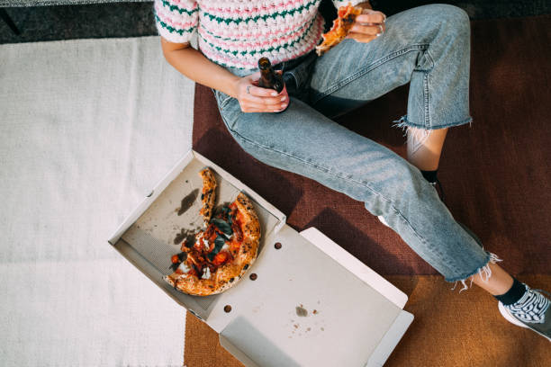 una mujer irreconocible comiendo pizza y bebiendo cerveza mientras está sentada en el suelo - young women sitting simple living eastern europe fotografías e imágenes de stock