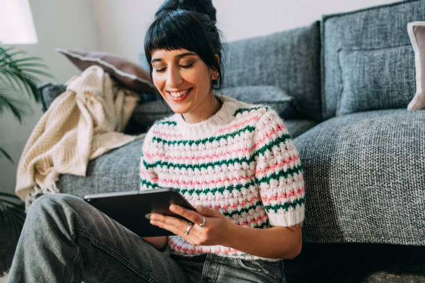 una hermosa mujer sosteniendo su tableta y viendo un divertido podcast - young women sitting simple living eastern europe fotografías e imágenes de stock