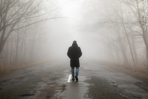 Fog landscape. Man walking  alone on scary foggy misty road.