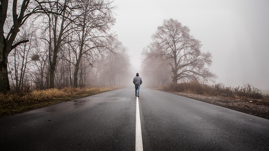 Lonly man  walk away into the misty foggy road in a dramatic mystic scene. Guy walking in a foggy autumn landscape
