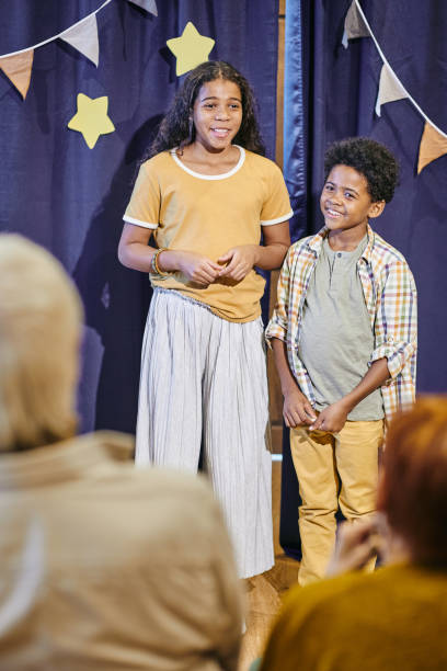 istock Happy siblings performing on stage against blue curtains 1357574519