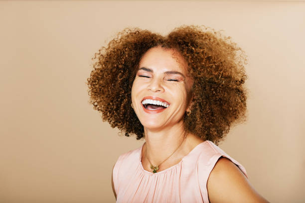 Fashion studio portrait of stylish middle age woman posing on beige background, laughing 50 - 55 year old lady with curly hair stock photo