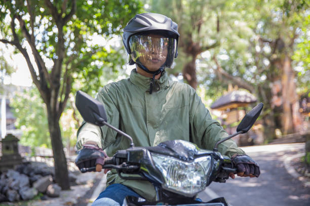Close-up shot of Indonesian man riding motorcycle on the street with a full face helmet. He's wearing protected gear such as helmets, a jacket, and gloves.