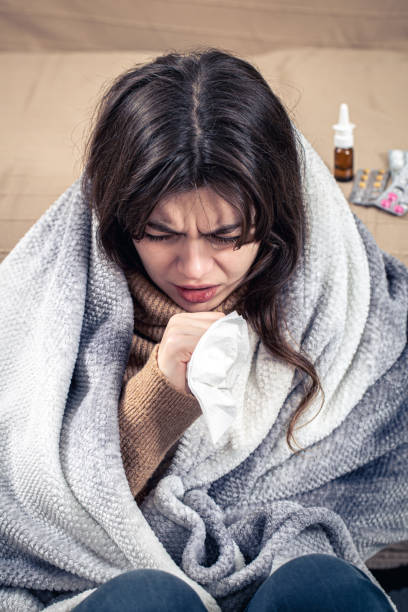 istock A young woman is coughing while sitting at home, wrapped in a blanket. 1357577194