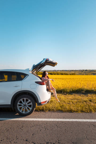 農場を見て日没時にsuvの車のトランクに座って笑顔かわいい女性 - tourism travel travel destinations vertical ストックフォトと画像