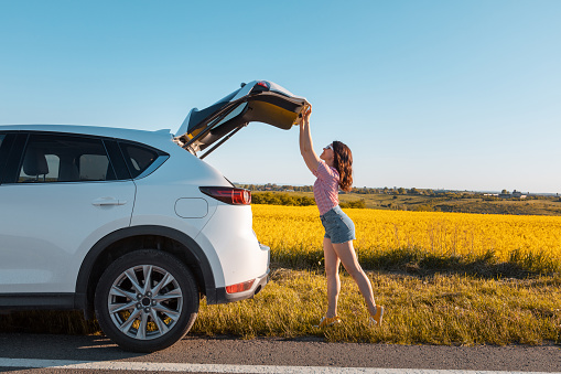 woman closing car trunk parked at roadside copy space