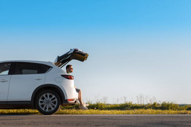 man sitting in car trunk enjoying view of sunset man sitting in car trunk enjoying view of sunset copy space sports utility vehicle stock pictures, royalty-free photos & images