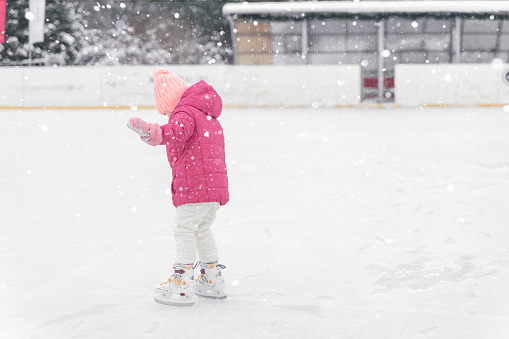 little girl in a red jacket is skating on a skating rink in heavy snow