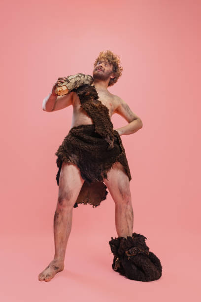 ganzkörperporträt eines lustigen mannes im charakter einer primitiven person, neandertaler in tierkleidung isoliert über rosa hintergrund - ethnisches erscheinungsbild stock-fotos und bilder
