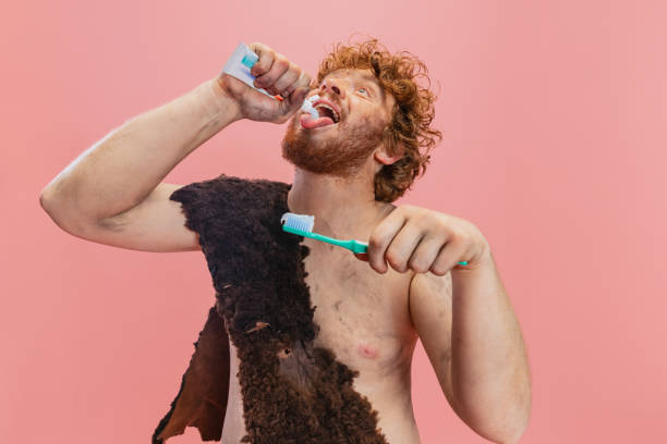 porträt eines mannes in charakter eines neandertalers, der tootpaste isoliert über rosa hintergrund in den mund drückt - ethnisches erscheinungsbild stock-fotos und bilder
