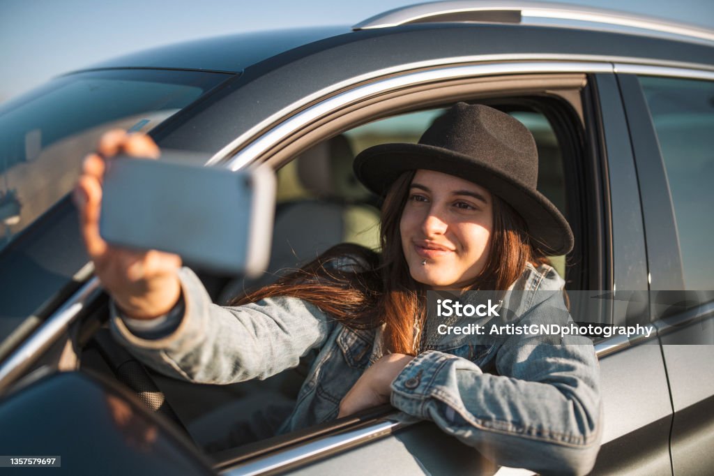 Portrait Of Smiling Woman Taking Selfie While Sitting In Car Portrait of smiling woman taking selfie while sitting in car Car Stock Photo