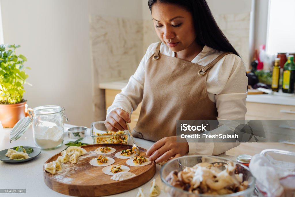 Beautiful Woman Preparing Healthy Meal in her Kitchen Smiling Asian woman filling dumpling gyoza wrappers on a wooden plate. Chef Stock Photo