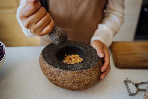 Close up photo of Asian woman hands grinding spices with pestle and mortar while standing in the kitchen.