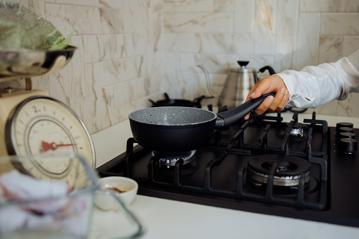 Close up photo of Asian woman hand places the pan on the stove in the kitchen.