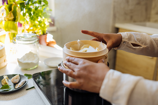 Close up photo of Asian woman hands putting bamboo steamer over a pot.