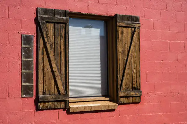 Old window with wooden shutters on the side of a red brick building