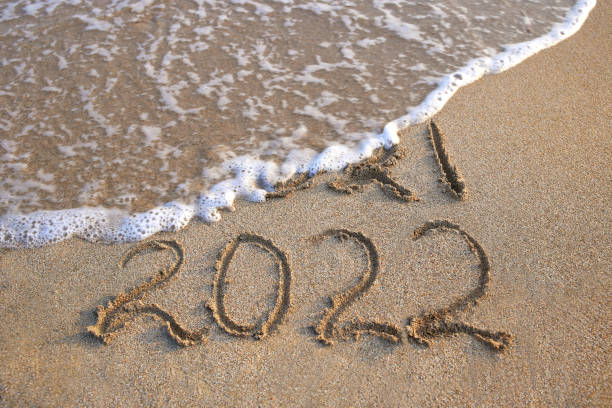 istock 2021, 2022 years written on sandy beach sea. Wave washes away 2021. 1357600752