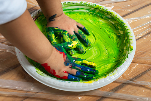 Caucasian child is playing with a plate full of finger painting color.
