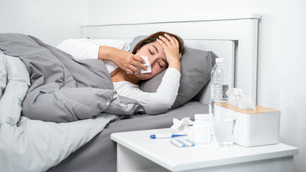 istock Asian woman using tissue to cough, sneezing and touching forehead while feeling sick and lying in blanket 1357606667