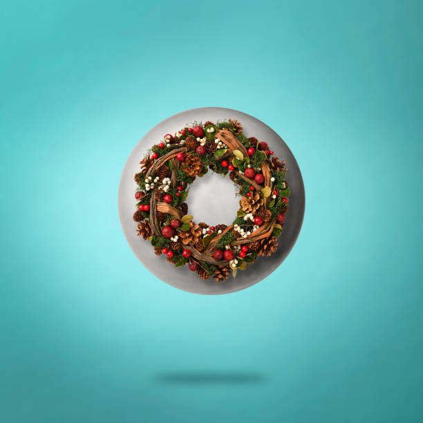Christmas Wreath and elliptical shape aluminum in mid-air against light blue background.
