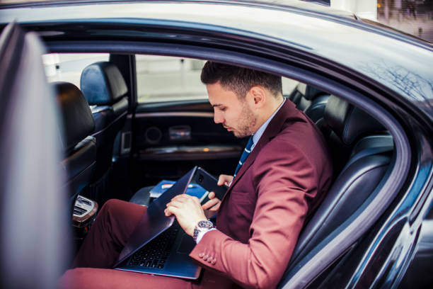 istock Serious businessman in purple suit using lap top in a car 1357614155