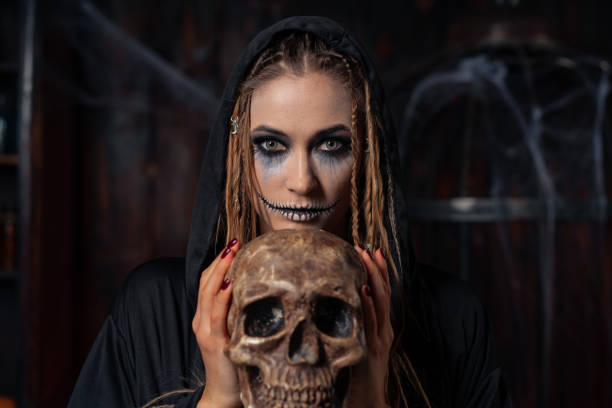 istock Halloween concept. Witch portrait close up with dreadlocks looking camera dressed black hood standing dark room with cage on background 1357618151