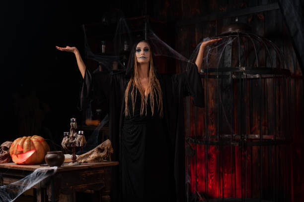 istock Halloween concept. Witch dressed black hood with dreadlocks standing dark dungeon room use magic book for conjuring magic spell 1357618158
