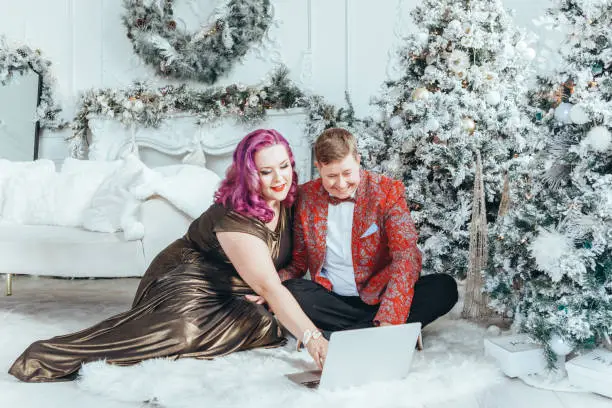 LGBTQ lesbian homosexual couple celebrating Christmas or New Year. Gay young lady female woman with butch partner calling friends and family online on laptop.
