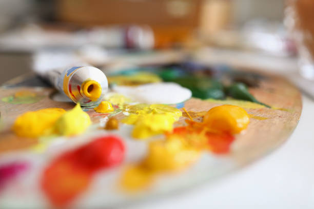Close-up of tube and mixed yellow and red paints on surface. Creamy oil paints on palette. Painter equipment for work. Masterpiece idea. Creativity flow. Artistry concept