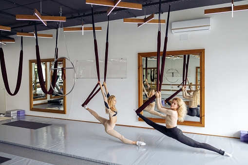 Two young flexible women doing aerial yoga in stretching studio in the daytime. Healthy lifestyle concept