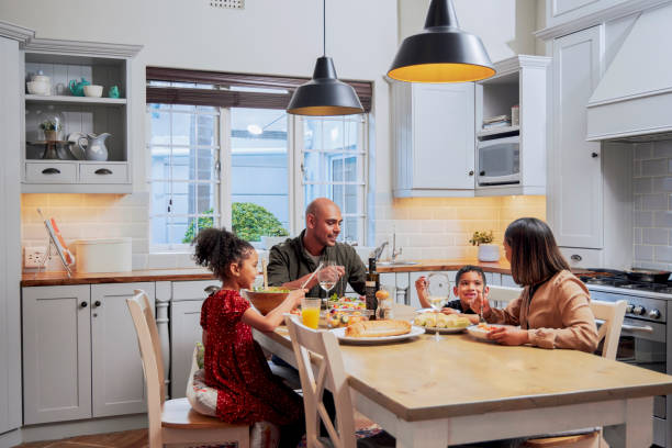 aufnahme einer jungen familie, die zusammen essen - two parent family indoors home interior domestic kitchen stock-fotos und bilder