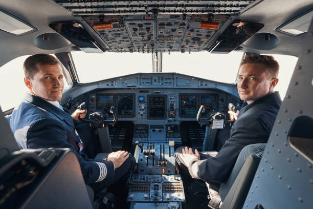 dos pilotos sentados en la cabina y mirando a la cámara - pilot cockpit flying business fotografías e imágenes de stock