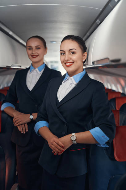 istock Two stewardesses standing on airplane aisle with folded hands 1357625055